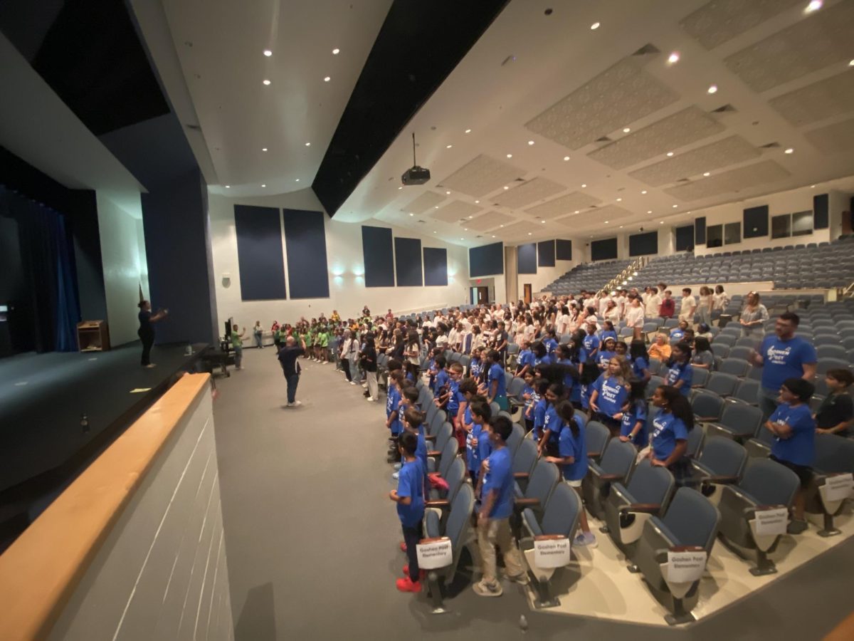 In the auditorium at Champe, choir students are practicing the National Anthem before the varsity football game. 