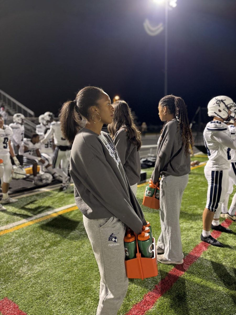 Football manager Ayda Pannell is standing on the sidelines of an away football game. She watched the game waiting for the players to need her assistance.
