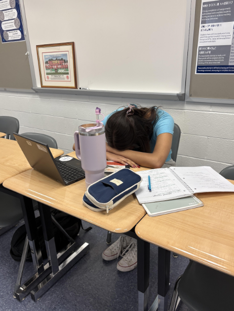 A student is struggling to finish her work during her study hall block. She was taking a break from the work surrounding her. 
